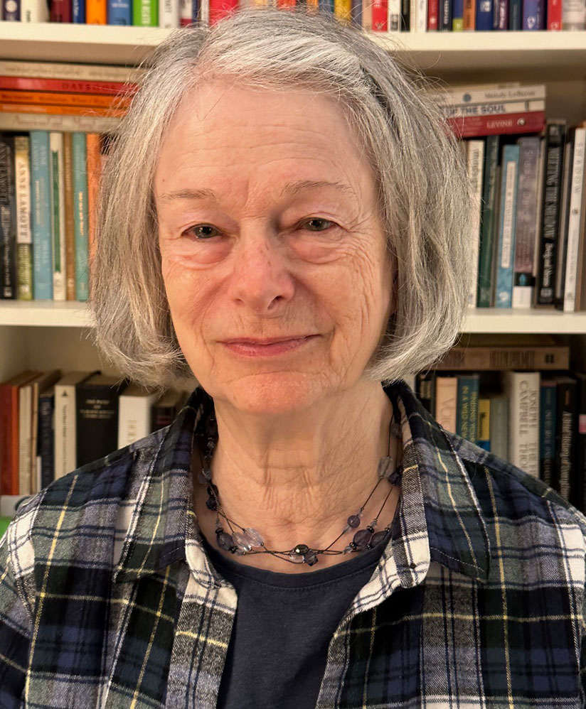 Head and shoulders photograph of Lynn Corrigan in front of a bookshelf filled with books.